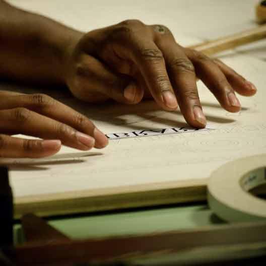 A student's hands working at a drafting table in Architecture class